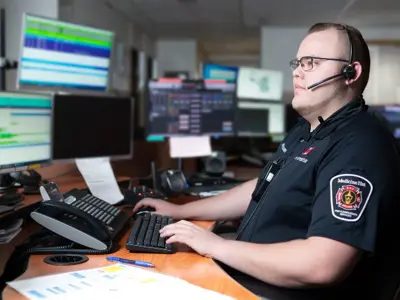 911 dispatch man with headset viewing computer screens
